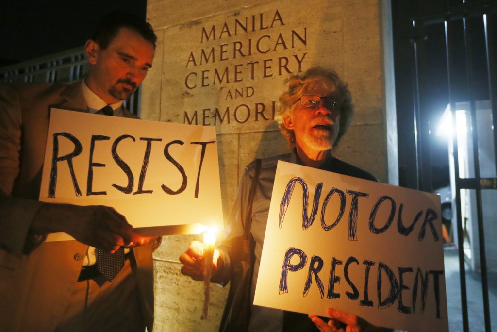 American residents in the Philippines Gabriel Ortiz, left, and Donald Goertzen display placards during a candlelight vigil at the American Cemetery to protest the inauguration of President-elect Donald Trump as the 45th President of the United States Friday, Jan. 20, 2017 in suburban Taguig city east of Manila, Philippines.(AP Photo/Bullit Marquez)