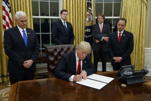 President Donald Trump, flanked by Vice President Mike Pence and Chief of Staff Reince Priebus, signs his first executive order on health care, Friday, Jan, 20, 2017, in the Oval Office of the White House in Washington. (AP Photo/Evan Vucci)